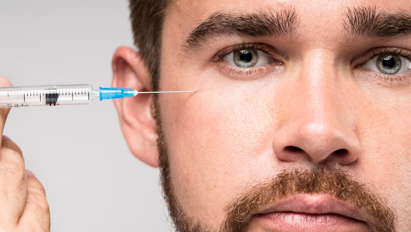 Man holding Botox syringe on his face
